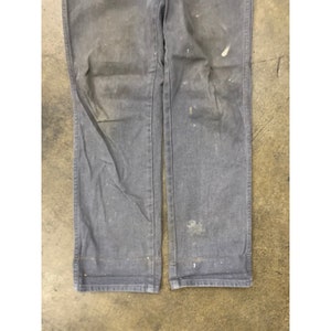 May include: A pair of dark gray work pants with visible wear and tear. The pants have a straight leg and a relaxed fit.