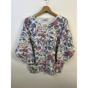 May include: A white floral patterned sweater with a round neckline. The sweater has a vintage look and is made of a soft, comfortable material.