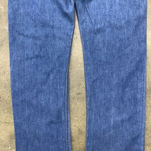 May include: A pair of blue denim jeans with a straight leg fit. The jeans have a classic five-pocket style and a button fly.