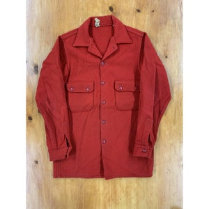 May include: A red long-sleeved shirt with a button-up front and two large pockets. The shirt is made of a thick, textured fabric.