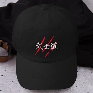 May include: Black baseball cap with the Japanese characters "Bushido" embroidered in white and red. The cap has a curved brim and a classic six-panel design. A stylish accessory for casual wear.