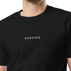 May include: Black t-shirt with the word "BUSHIDO" printed in white across the chest. The shirt has short sleeves and a crew neck. The text is centered and in a simple sans-serif font.