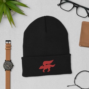 Puede incluir: Gorro negro con un logotipo de zorro rojo bordado en la parte delantera. El logotipo es un zorro estilizado con alas.