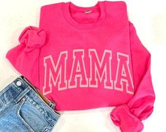 May include: Pink sweatshirt with a white outline of the word "MAMA" in a collegiate font.
