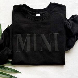 May include: Black sweatshirt with the word "MINI" printed in a bold, raised font.