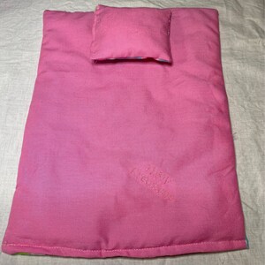 Puede incluir: Una cama de mu&ntilde;eca rosa con una almohada rosa a juego. La cama est&aacute; bordada con el texto "Pink Creations".