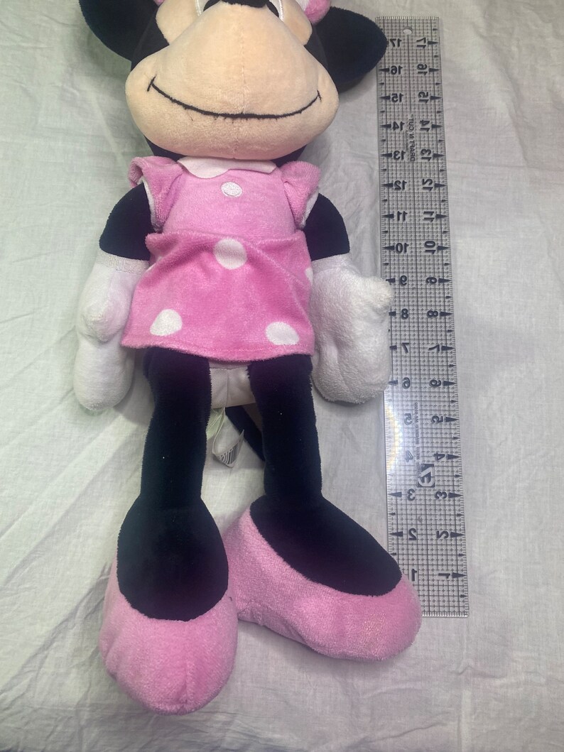 Puede incluir: Un juguete de peluche rosa y negro de un rat&oacute;n de dibujos animados que lleva un vestido rosa con lunares. El juguete mide aproximadamente 76 cm de alto.