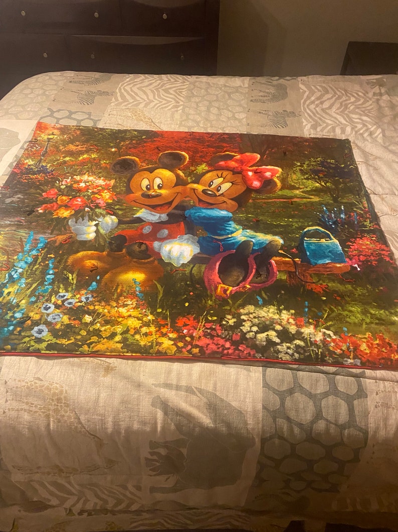 Puede incluir: Un tapiz colorido con Mickey Mouse y Minnie Mouse en un entorno de jard&iacute;n. El tapiz es una mezcla vibrante de verdes, rojos, amarillos y azules, con flores y follaje que rodean a los ic&oacute;nicos personajes de Disney.