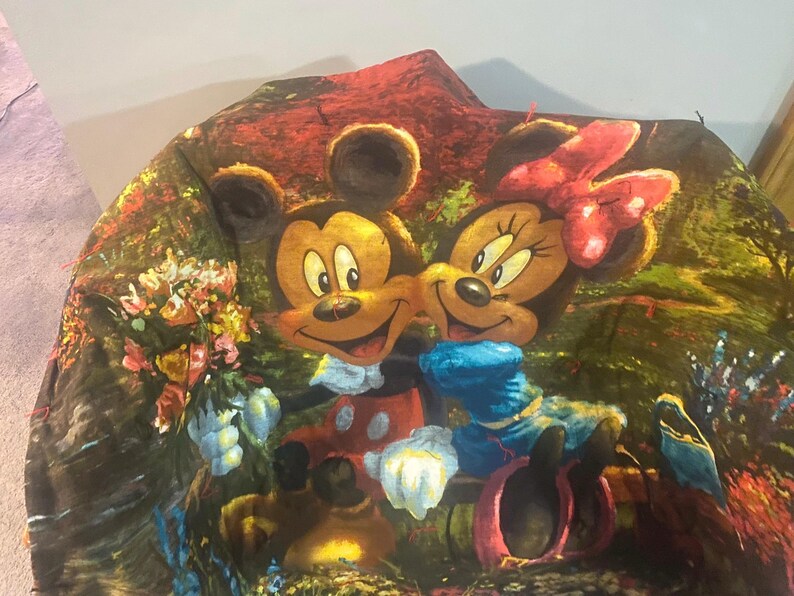 Puede incluir: Una tela colorida con Mickey Mouse y Minnie Mouse en un entorno de jard&iacute;n. La tela tiene un fondo verde, marr&oacute;n y rojo con flores y plantas.