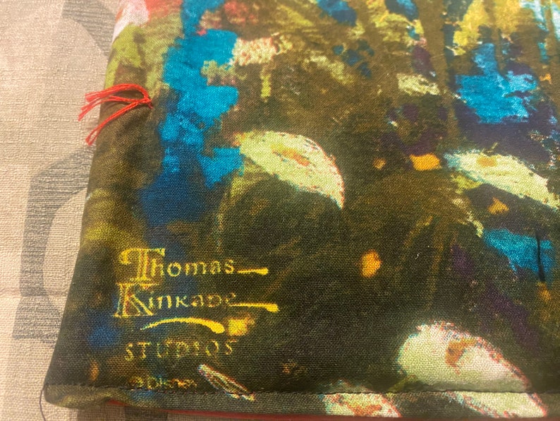 Puede incluir: Primer plano de una tela verde oscura con un dise&ntilde;o abstracto azul y amarillo. La tela tiene una etiqueta bordada en oro que dice "Thomas Kinkade Studios".
