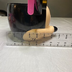 Puede incluir: Cubo de pl&aacute;stico negro con forma de personaje de Mickey Mouse con un asa rosa. El cubo mide aproximadamente 15 cm de alto.