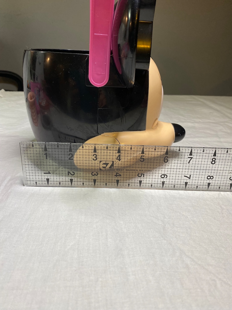 Puede incluir: Cubo de pl&aacute;stico negro con forma de personaje de Mickey Mouse con un asa rosa. El cubo mide aproximadamente 15 cm de alto.