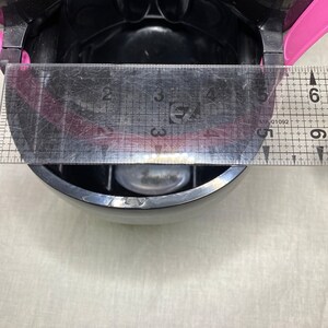 Puede incluir: Un recipiente de pl&aacute;stico negro con una tapa rosa y una regla transparente que mide 15 cm. El recipiente tiene una peque&ntilde;a tapa redonda transparente en el interior.