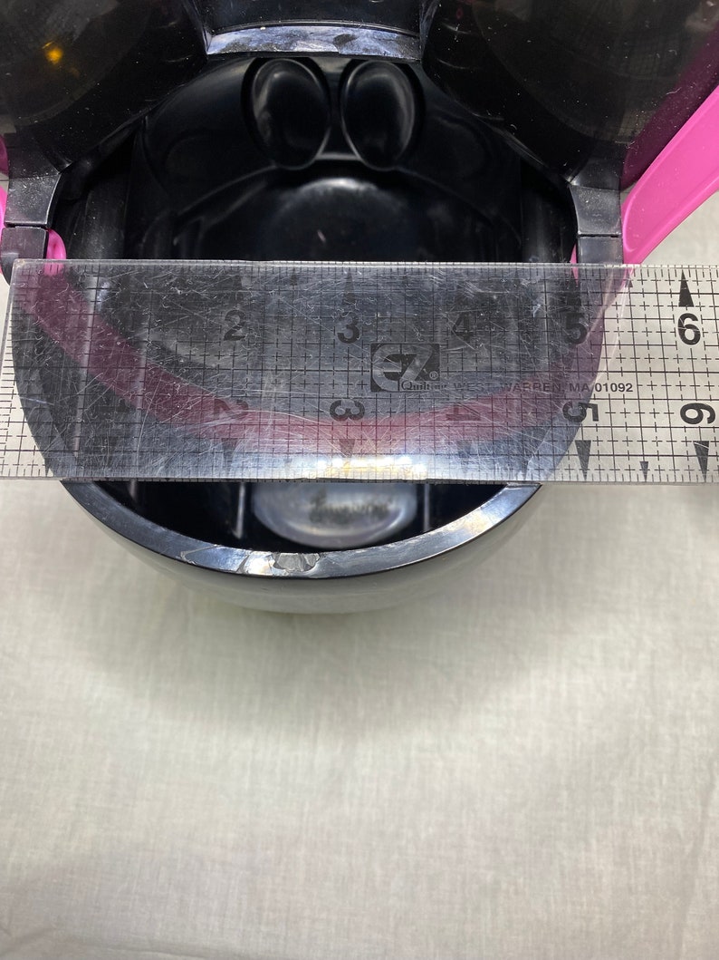 Puede incluir: Un recipiente de pl&aacute;stico negro con una tapa rosa y una regla transparente que mide 15 cm. El recipiente tiene una peque&ntilde;a tapa redonda transparente en el interior.