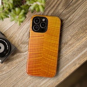 May include: A wooden phone case with a warm, amber-colored finish and a natural wood grain pattern. The case has a glossy finish and a camera cutout. The phone case is on a wooden surface.
