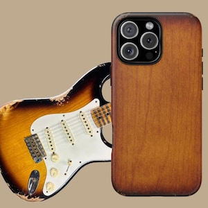 Puede incluir: Funda de teléfono con textura de madera y diseño de guitarra. La funda tiene un acabado marrón con un aspecto envejecido. Una guitarra eléctrica de estilo vintage con acabado sunburst es parcialmente visible detrás de la funda, añadiendo un tema musical.
