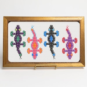 May include: Four colorful embroidered lizards in a gold frame. The lizards are purple, orange, black, and red.