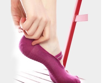 Puede incluir: Un par de calcetines antideslizantes de color morado con una correa en la parte superior del pie. Las calcetines están siendo puestos por una mano.