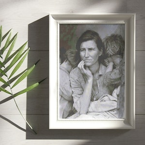 May include: A black and white photograph of a woman holding a young child. The woman is looking off to the side with a thoughtful expression. The child is looking down and has their arms wrapped around the woman's waist. The photograph is framed in a white frame.