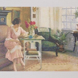 Pode incluir: Uma mulher de vestido rosa está sentada à mesa em um quarto ensolarado. Ela está lendo um livro e há um vaso com flores vermelhas na mesa.