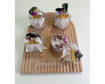 May include: Four small glass jars with lids, filled with dried flowers and a white ribbon. The jars are arranged on a wooden tray with a curved edge. The tray has a light brown wood grain and a white inscription that reads "fkcreations.net".