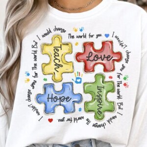 May include: White sweatshirt with a colorful puzzle design. The puzzle pieces spell out "Teach, Love, Hope, Inspire." Surrounding text reads "I would change the world for you. I wouldn't change you for the world."
