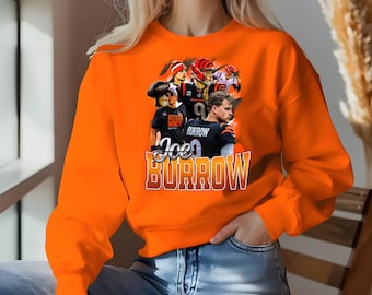 Puede incluir: Sudadera naranja con un estampado gráfico de Joe Burrow y otros jugadores de los Cincinnati Bengals. El texto "Joe Burrow" está impreso en letras grandes y en negrita.