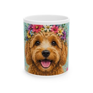 May include: White ceramic mug featuring a watercolor illustration of a golden doodle dog wearing a flower crown. The dog has a happy expression with its tongue out. The background is a light blue with colorful floral accents.