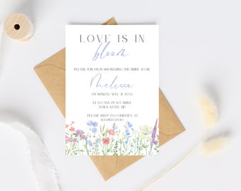May include: A white card with a floral border and the text "LOVE IS IN bloom" in black and blue. The text "PLEASE JOIN US IN SHOWERING THE BRIDE TO BE Melissa ON SUNDAY MAY 21, 2023 AT 123 ANY PLACE DRIVE TOWN STATE ZIP PLEASE RSVP TO COURTNEY AT (555) 555-5555" is printed in black.