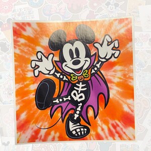 May include: A square sticker featuring Mickey Mouse in a Halloween costume. Mickey is dressed as a skeleton with a purple cape and a green bow tie, set against an orange and white tie-dye background.