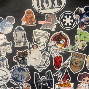 May include: A collection of Star Wars themed stickers featuring characters like Chewbacca, Yoda, and Darth Vader. The stickers include text such as "#SQUADGOALS", "May the 4th with you", and "I'm your father". The stickers are in various shapes and sizes.
