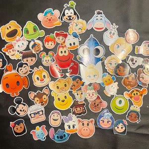 Puede incluir: Una colección de pegatinas de personajes de dibujos animados coloridos con varios personajes de Disney. Las pegatinas incluyen personajes de películas como Buscando a Nemo, Frozen y Toy Story. Las pegatinas son de varios tamaños y formas.