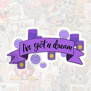 May include: A purple sticker with the phrase "I've got a dream" in black script. The sticker features purple cylinders and spheres, with yellow accents. The background is filled with various colorful stickers.