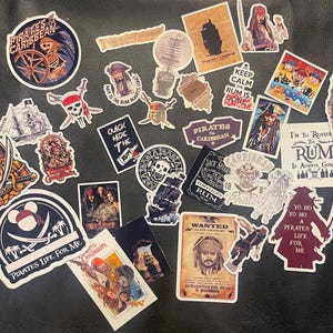 Puede incluir: Una colección de pegatinas con temática pirata que presentan calaveras, espadas, barcos y personajes de la serie de películas Piratas del Caribe. Las pegatinas tienen varias formas y tamaños, con textos como "Pirates Life For Me" y "I'm the reason the rum is always gone."