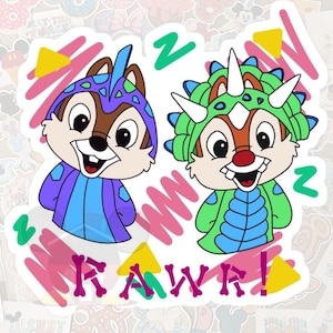 May include: Two cartoon chipmunks wearing dinosaur costumes. One is in purple and blue, the other in green and blue. The word "RAWR!" is written in pink with yellow triangles and green zigzags. The background is filled with various stickers.
