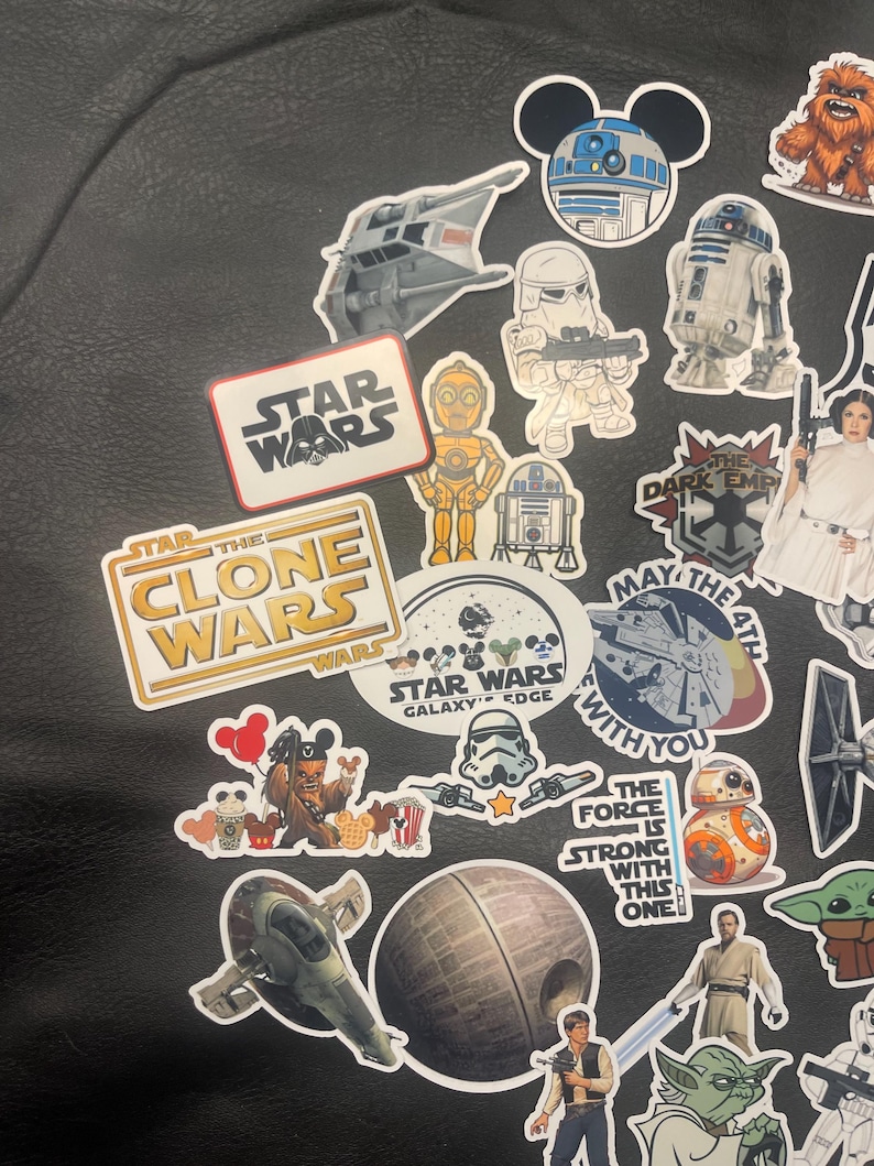 May include: A collection of Star Wars themed stickers featuring characters like R2-D2, C-3PO, and Yoda. The stickers include various designs, including the Star Wars logo, the Death Star, and the Millennium Falcon. The stickers are on a black surface.