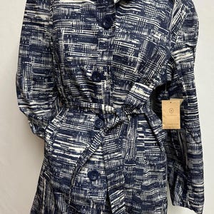 May include: A navy blue and white long-sleeve jacket featuring a textured abstract grid pattern. The jacket has a collared neckline, a front button closure, and a matching fabric tie belt at the waist. A small tan tag is attached to the side.