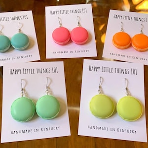 Peut inclure: Quatre paires de boucles d'oreilles macarons faites à la main sur des cartes blanches avec le texte "HAPPY LITTLE THINGS 101" et "HANDMADE IN KENTUCKY". Les boucles d'oreilles sont en quatre couleurs : sarcelle, rose, orange et vert.