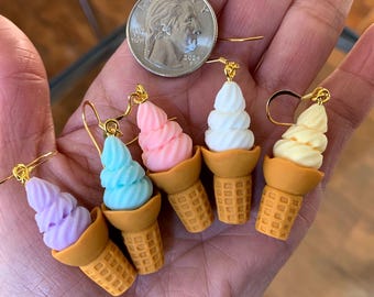 Op de afbeelding: Een set van zes ijshoorntjes oorbellen. De oorbellen zijn gemaakt van polymer clay en hebben verschillende kleuren ijs, waaronder paars, blauw, roze, wit en geel. Elke oorbel heeft een gouden haak.