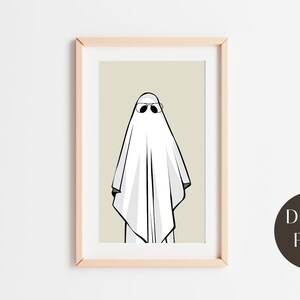 May include: A digital print of a white ghost wearing sunglasses against a beige background. The print is framed in a light wood frame.