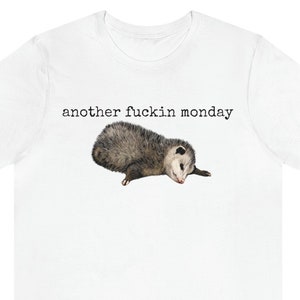 May include: White t-shirt with the text "another fuckin monday" printed in black. A small opossum is lying on its side below the text.