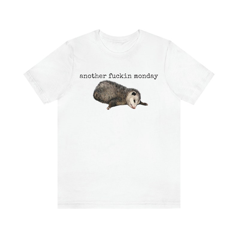 May include: White t-shirt with the text "another fuckin monday" printed in black. A small opossum is lying on its side below the text.