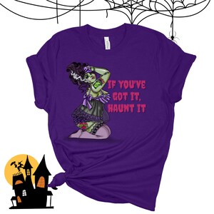 May include: Purple t-shirt with a green zombie woman wearing a black and purple lingerie outfit. The text "If you've got it, haunt it" is printed on the shirt.