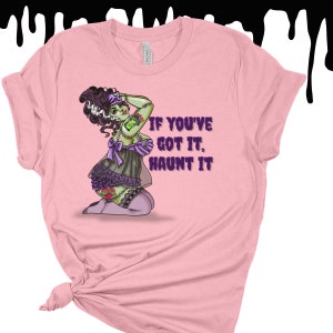 May include: Pink t-shirt with a green and purple illustration of a zombie woman in a lingerie outfit. The text "If you've got it, haunt it" is printed on the shirt.