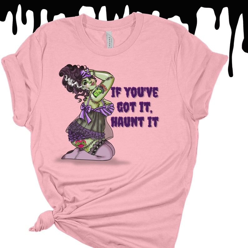 May include: Pink t-shirt with a green and purple illustration of a zombie woman in a lingerie outfit. The text "If you've got it, haunt it" is printed on the shirt.