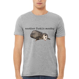 May include: A grey t-shirt with the text "another fuckin monday" and a small opossum lying down on the front.