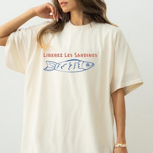 May include: A white oversized t-shirt with a blue and red graphic of a fish and the text "LIBEREZ LES SARDINES".