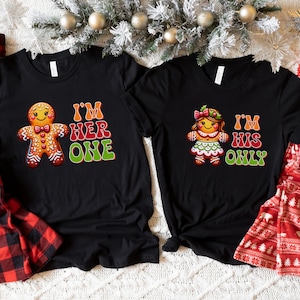 May include: Two black t-shirts with a gingerbread person graphic and the text "I'm Her One" and "I'm His Only".
