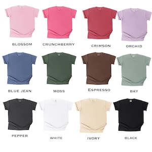 K&ouml;nnte beinhalten: Eine Sammlung von 12 leeren T-Shirts in verschiedenen Farben, darunter Bl&uuml;te, Crunchberry, Crimson, Orchidee, Blue Jean, Moos, Espresso, Bucht, Pfeffer, Wei&szlig;, Elfenbein und Schwarz.