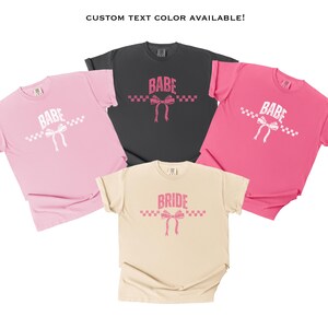 May include: Three t-shirts with a checkered pattern and a pink bow. The shirts say "Babe" and "Bride" in white text.